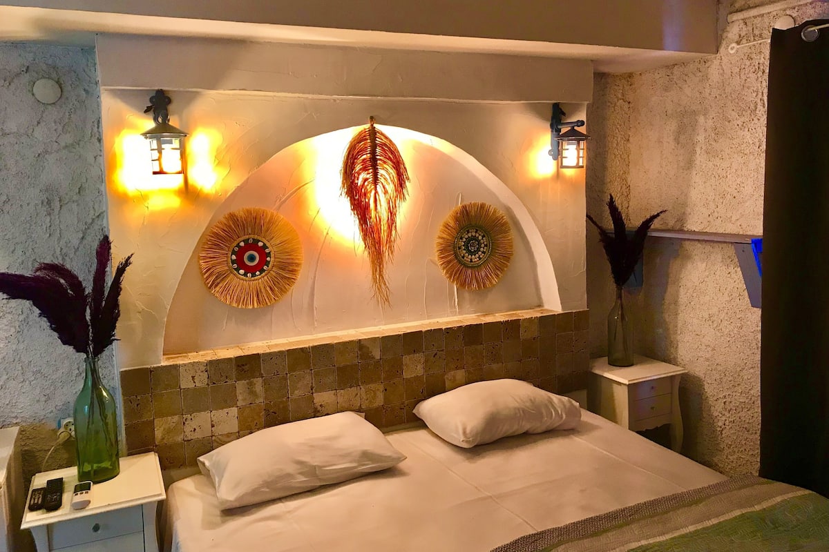 A bedroom with a bed, bedside tables, decorative wall art, and wall-mounted lights.