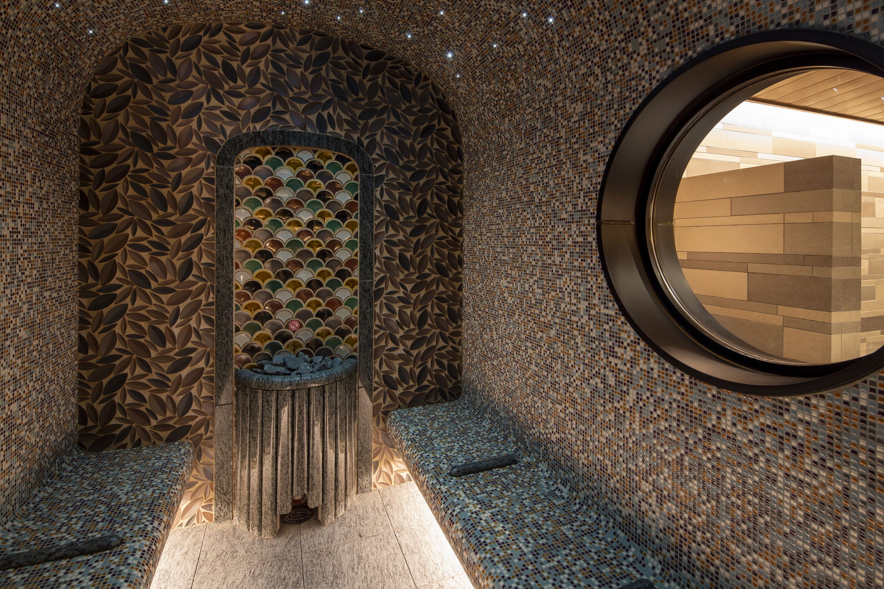 A spa area with a mosaic wall, a circular window, and a seating area.