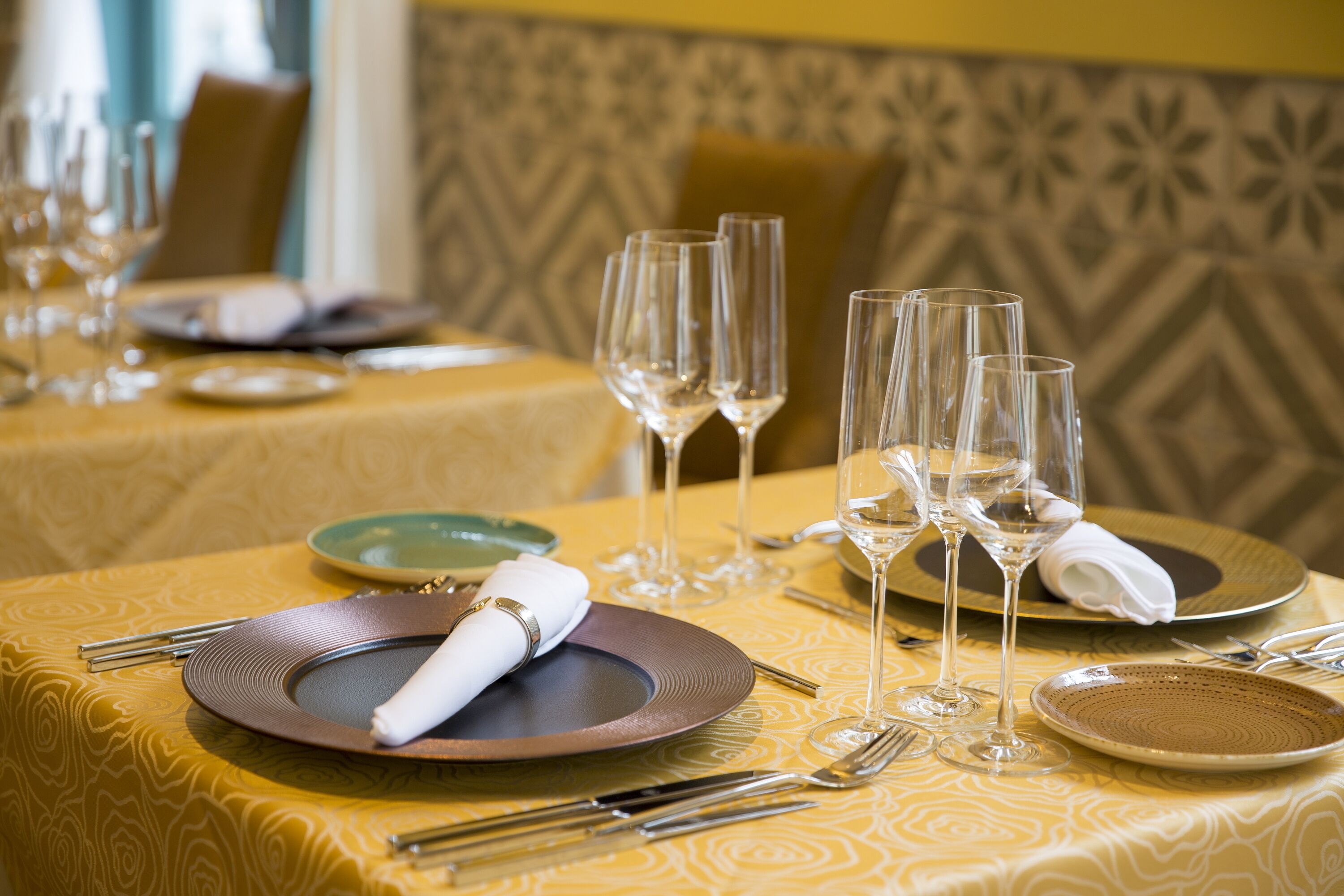 A dining table set with plates, cutlery, and wine glasses, indicating a formal dining arrangement.