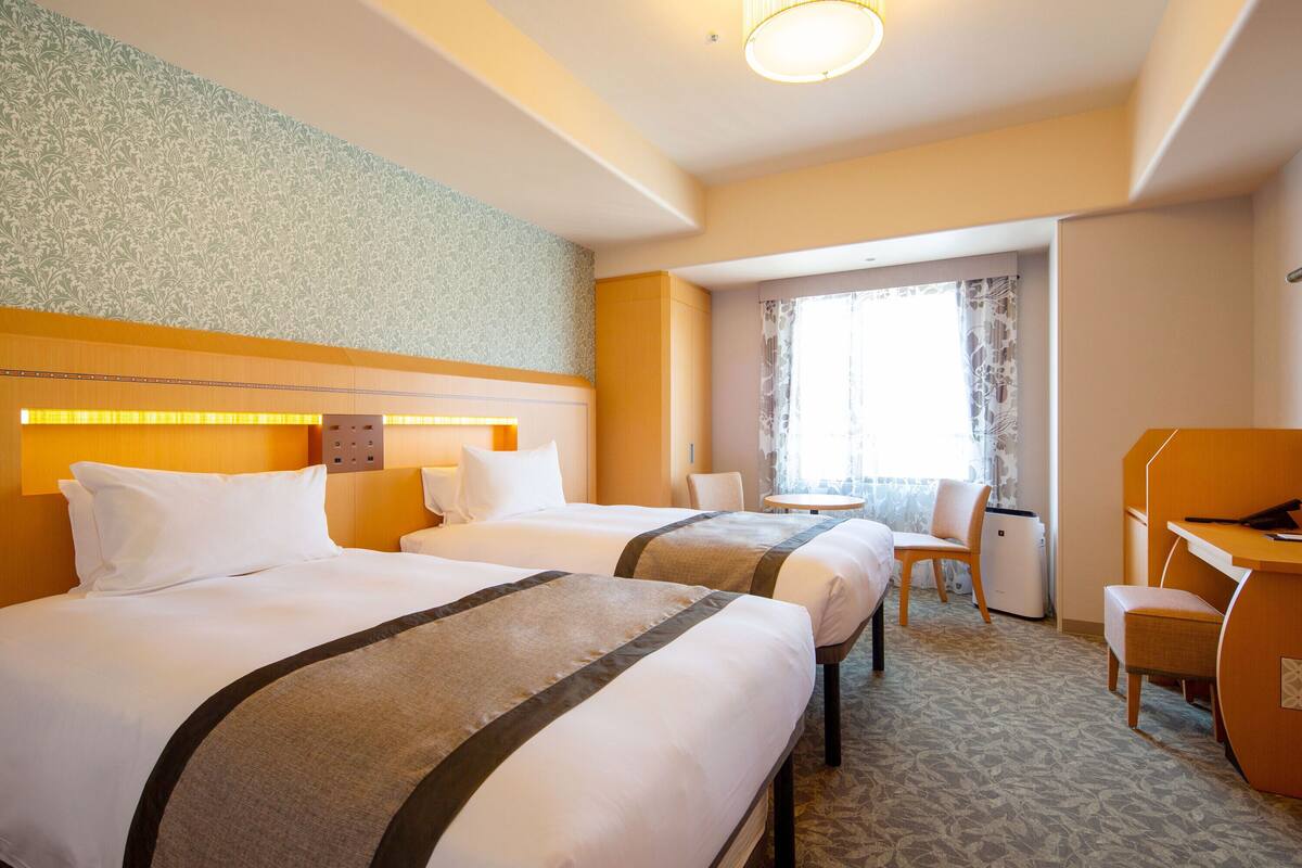 A hotel room with two beds, a desk, a chair, and a small table.