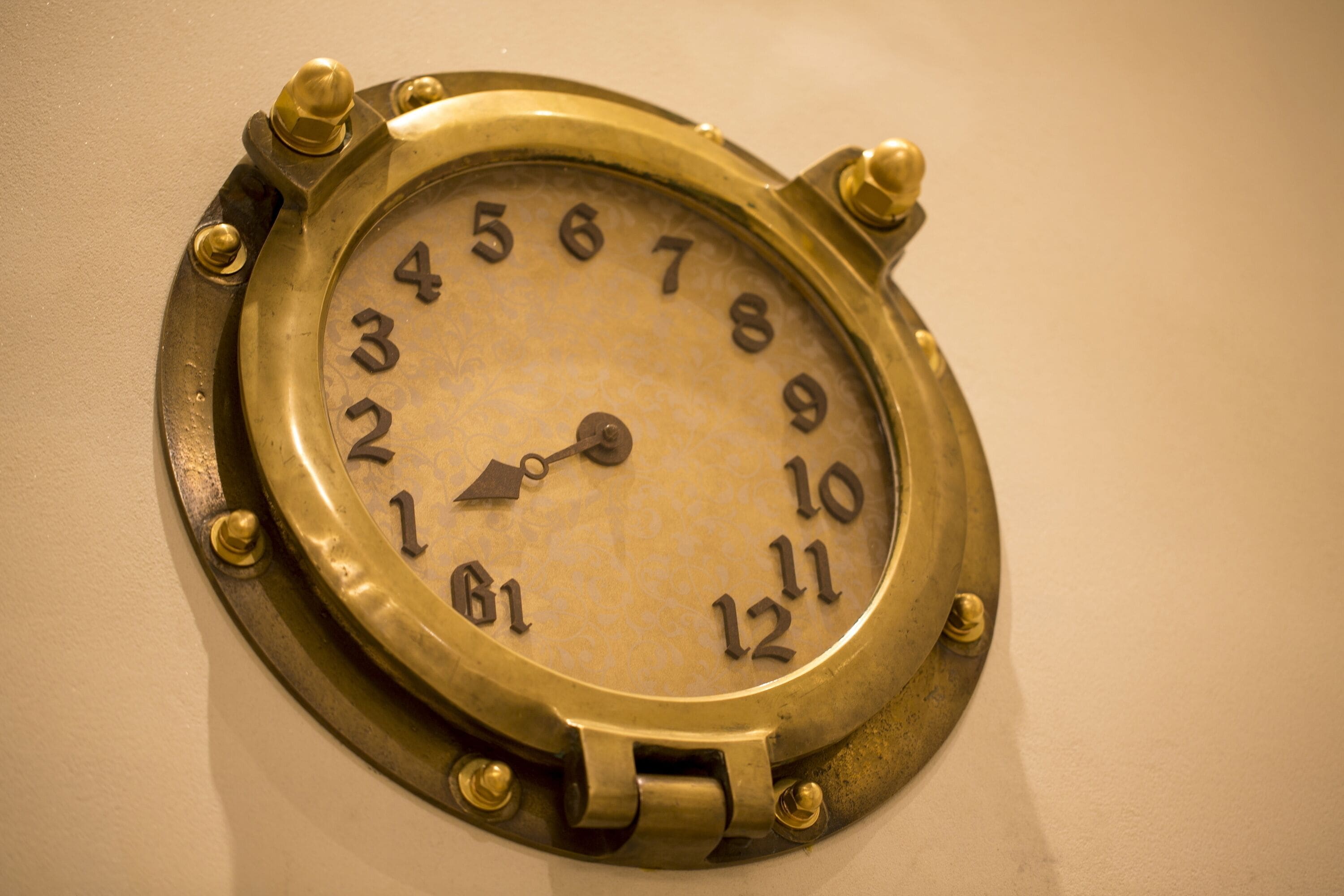 A brass clock with Roman numerals on a wall.