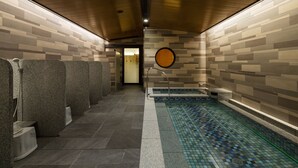 A modern bathroom with a tiled floor, a small pool, and a row of individual shower stalls. - Hotel Monterey KOBE (Kobe)