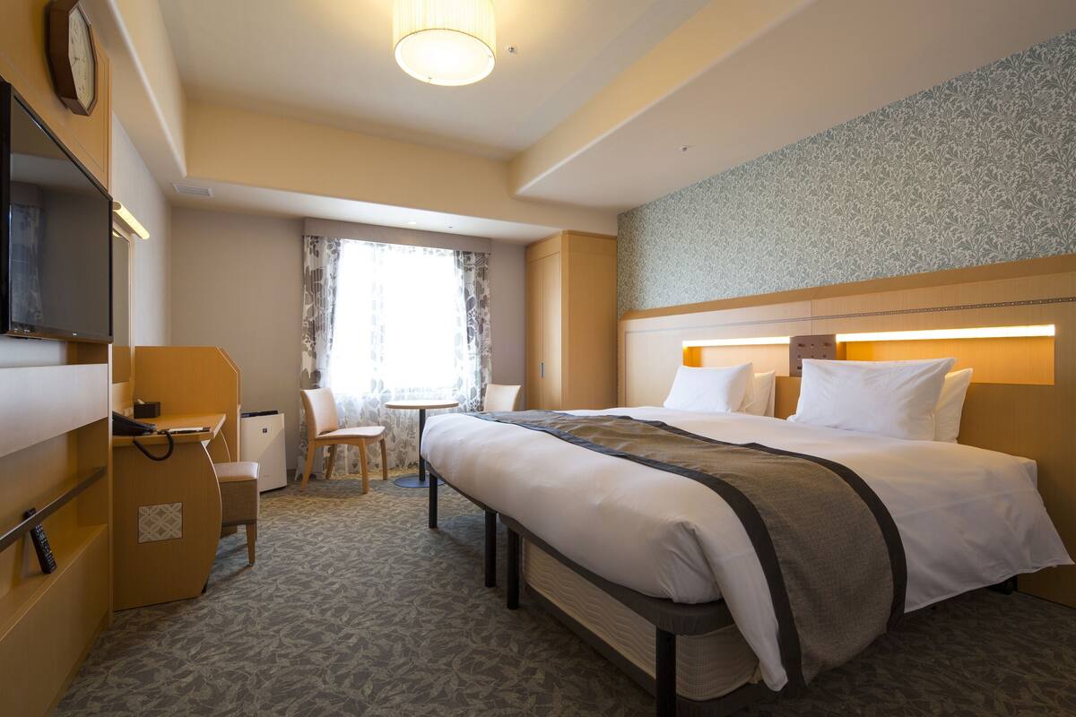 A hotel room with a bed, desk, chair, and a small table.