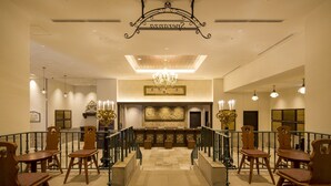 A lobby with a central staircase, wooden chairs, a chandelier, and a reception desk. - Hotel Monterey KOBE (Kobe)