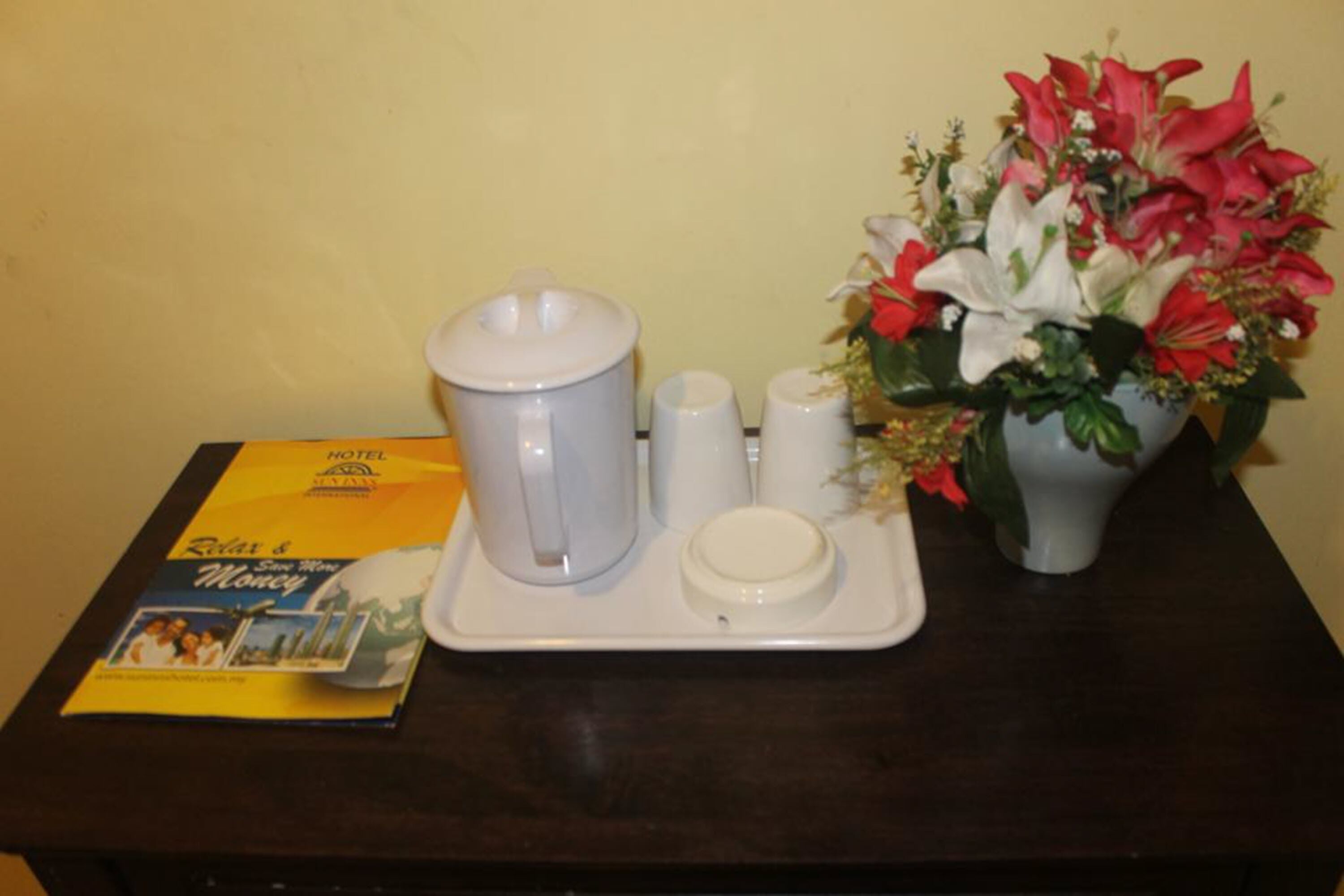 Un vassoio con una caffettiera, zucchero a cubetti e un brocchettino sul tavolo, accanto a una brochure e un vaso di fiori.
