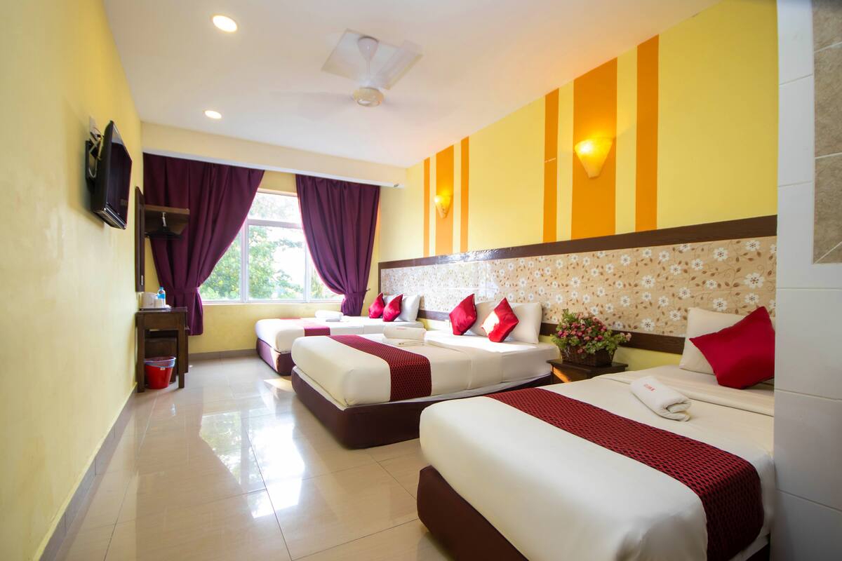 Quarto de hotel com duas camas, televisão, janela com cortinas roxas e parede com listras verticais.