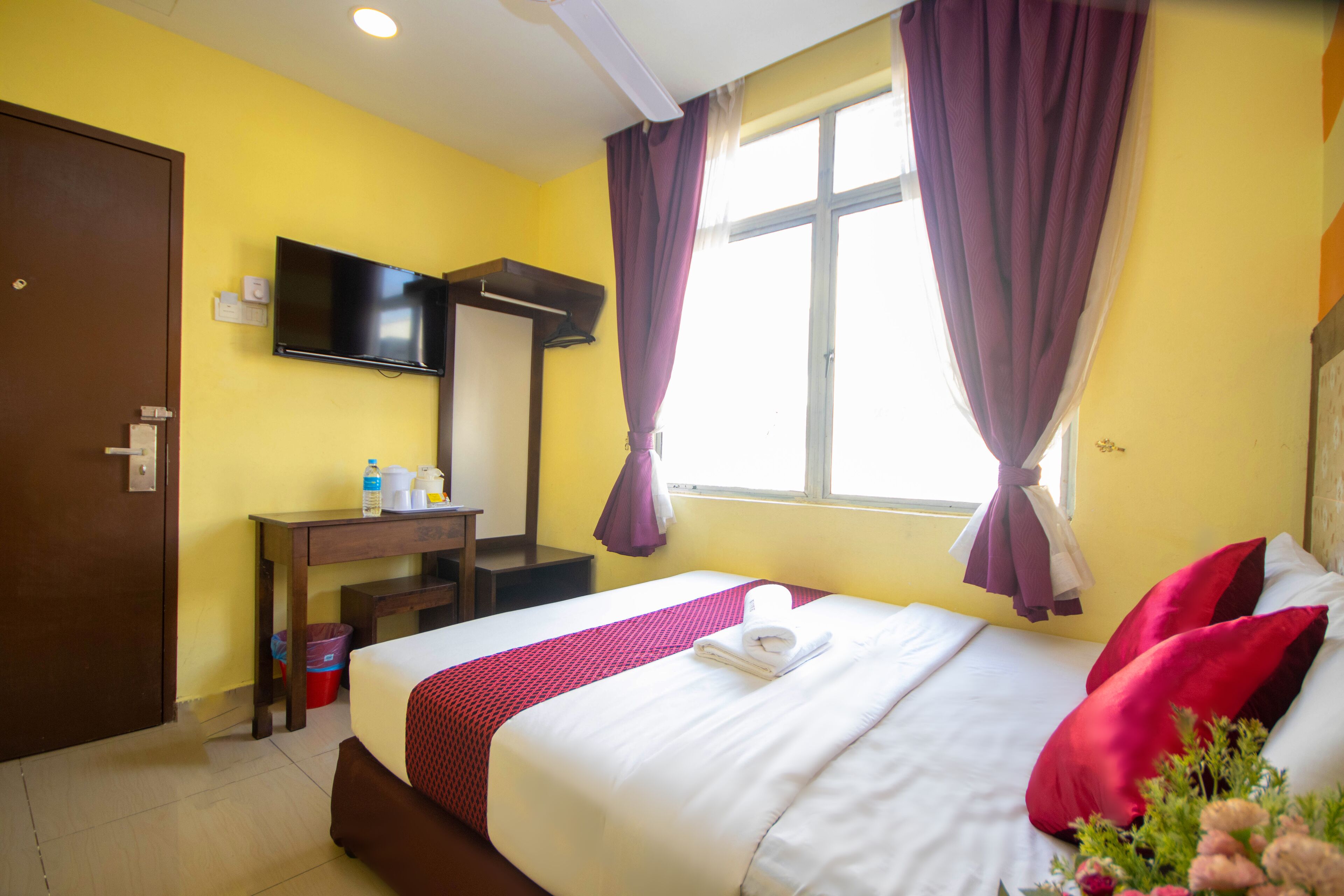 A hotel room with a bed, a desk, a television, and a window with curtains.