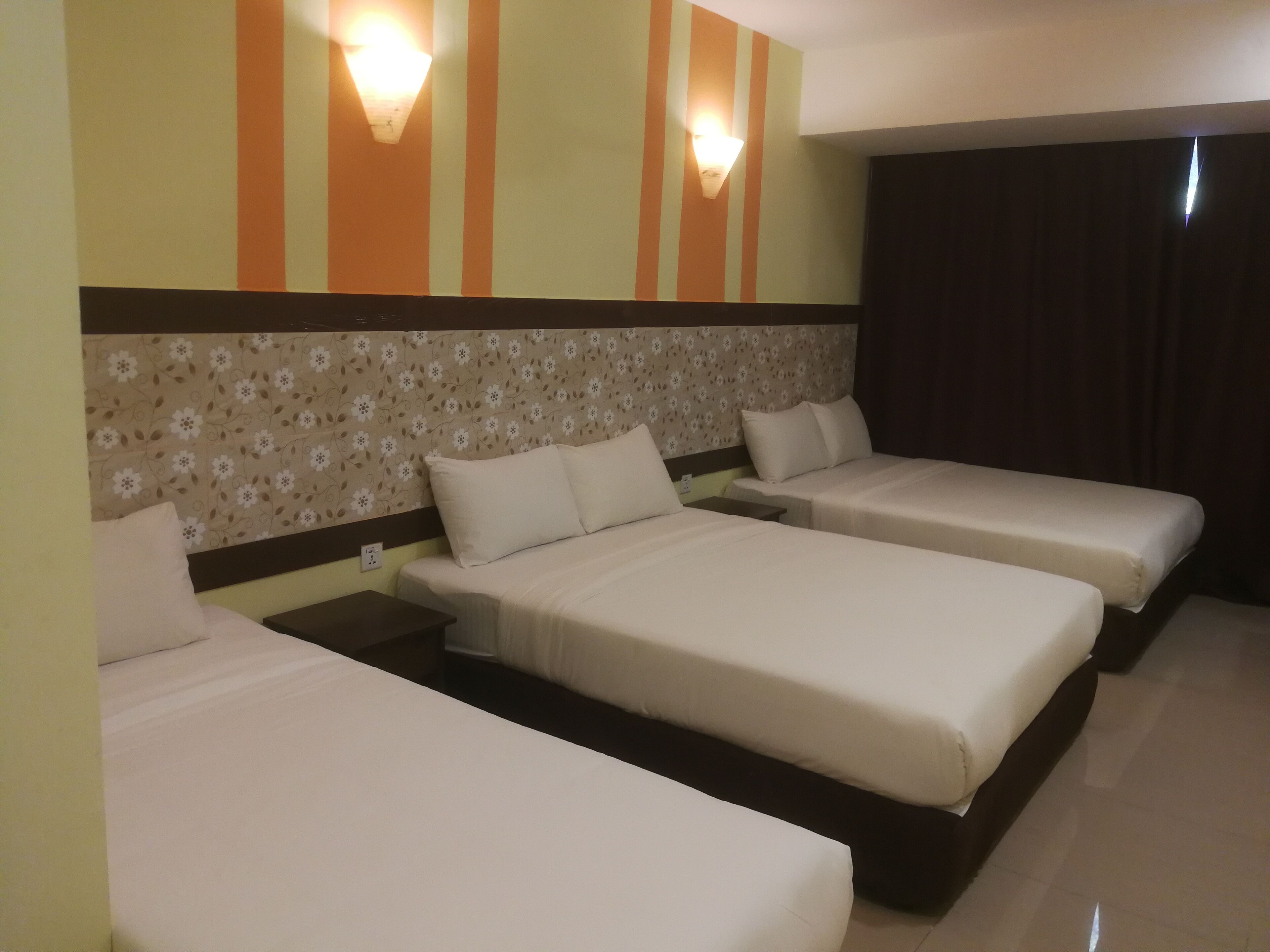 Habitación de hotel con tres camas individuales, cabecera estampada con motivos florales e iluminación en la pared.