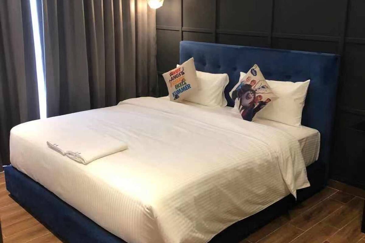 A hotel room with a large bed, dark headboard, and a wooden floor.