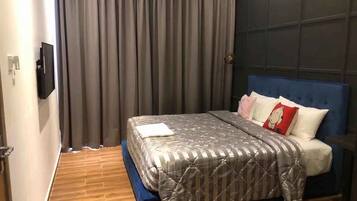 Un dormitorio con cama, cortinas, televisor y cabecera azul.