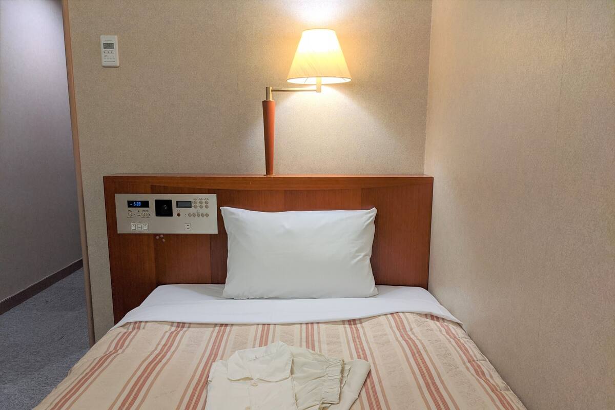 A hotel room with a bed, a control panel, a lamp, and a folded garment on the bed.