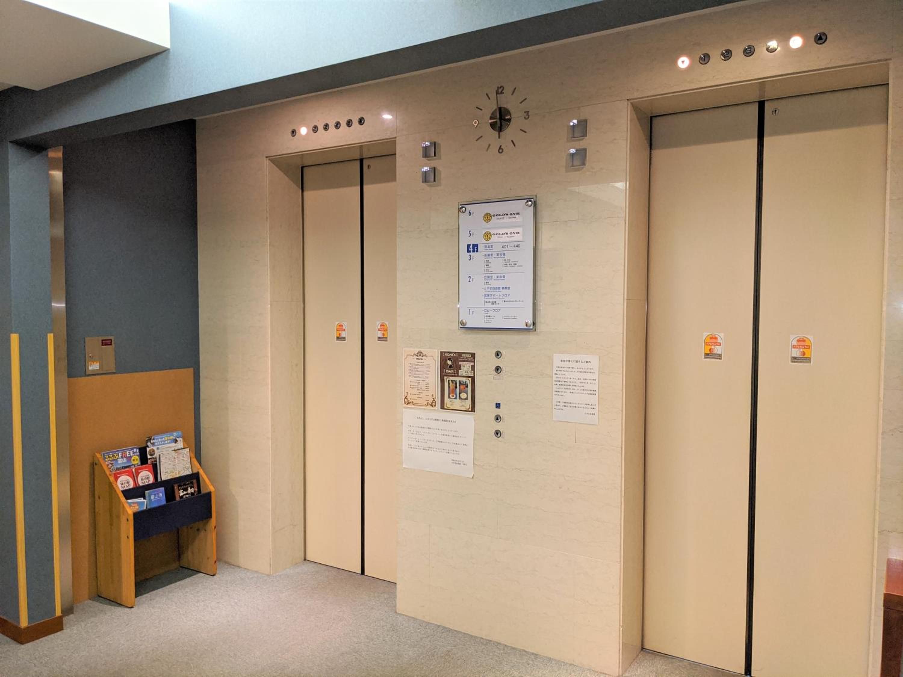 An elevator with a clock, emergency instructions, and a small display stand with brochures.