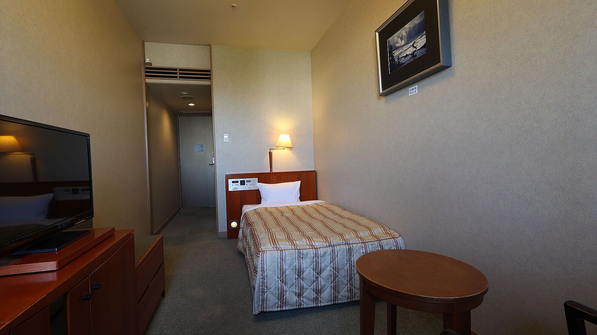 Habitación de hotel con cama, mesita de noche, televisión y una pequeña mesa redonda.