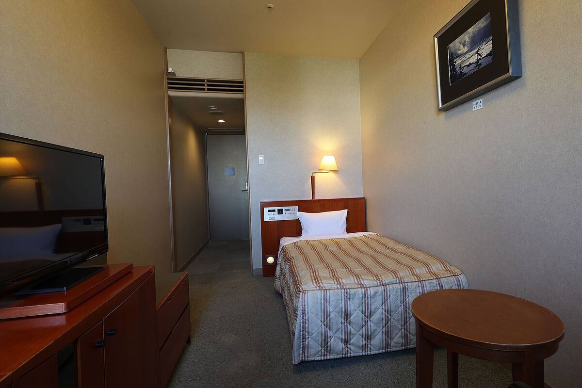 A hotel room with a bed, bedside table, TV, and a small round table.