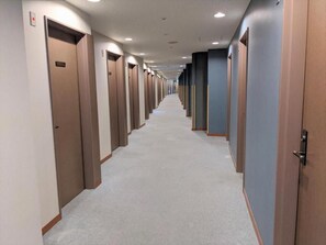 A hotel hallway with multiple doors, carpeted flooring, and recessed lighting. - Toyama Jiyukan (Toyama)