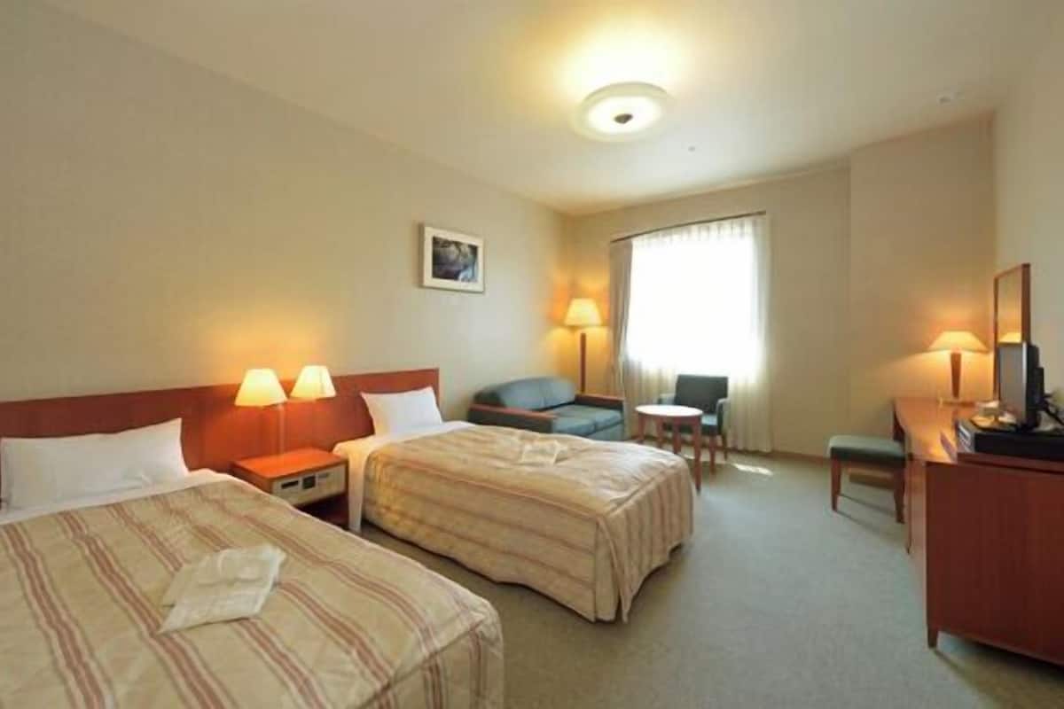 A hotel room with two beds, a desk, a chair, and a small table.