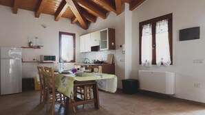 A kitchen with wooden beams, a dining table with chairs, a refrigerator, a microwave, and a window with curtains. - Residences Gattopardu- "Gone with the Wind" (Castiadas)