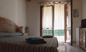 Un dormitorio con cama, cómoda, televisor y vista al exterior.