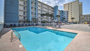 A swimming pool with a metal ladder, surrounded by lounge chairs and a white fence. - Bright Gulf Shores Beachfront Condo w/ Pool Access (Gulf Shores)
