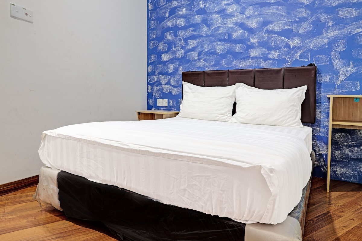 A neatly made bed with white bedding, a wooden headboard, and a nightstand with a small wooden table beside it.