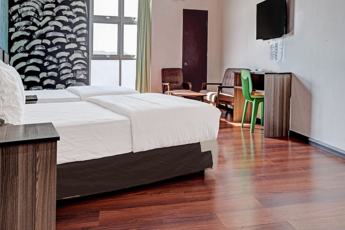 A hotel room with a large bed, a desk, a chair, and a television on the wall.