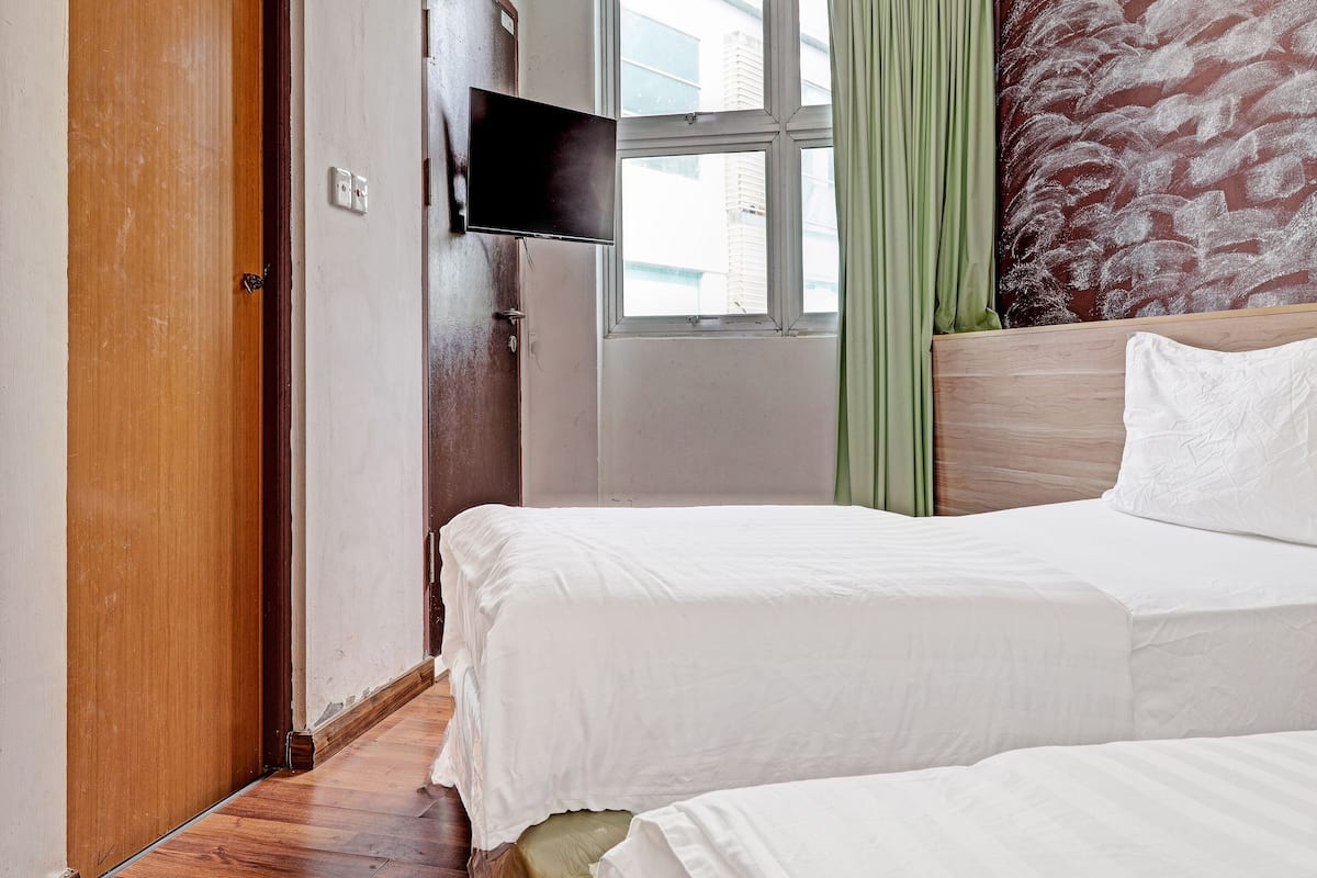 A bedroom with two beds, a wooden wardrobe, a television, and a window with curtains.