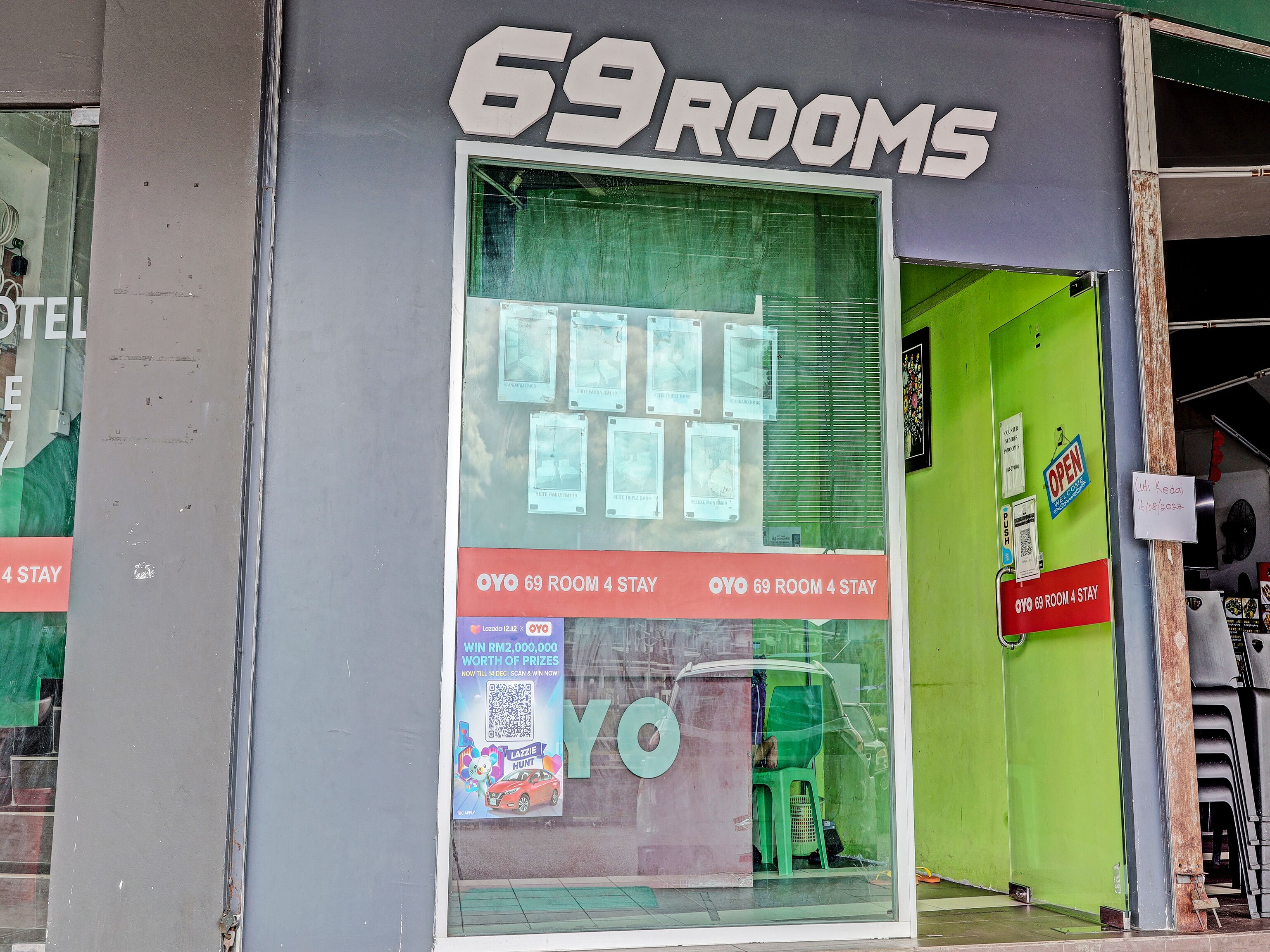 L'ingresso di un hotel con un grande cartello che indica "69 ROOMS" e una vetrina che mostra immagini di camere e un codice QR per una promozione.
