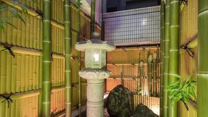 Un jardín japonés tradicional con un farol de piedra, bambú y un muro de tejas.