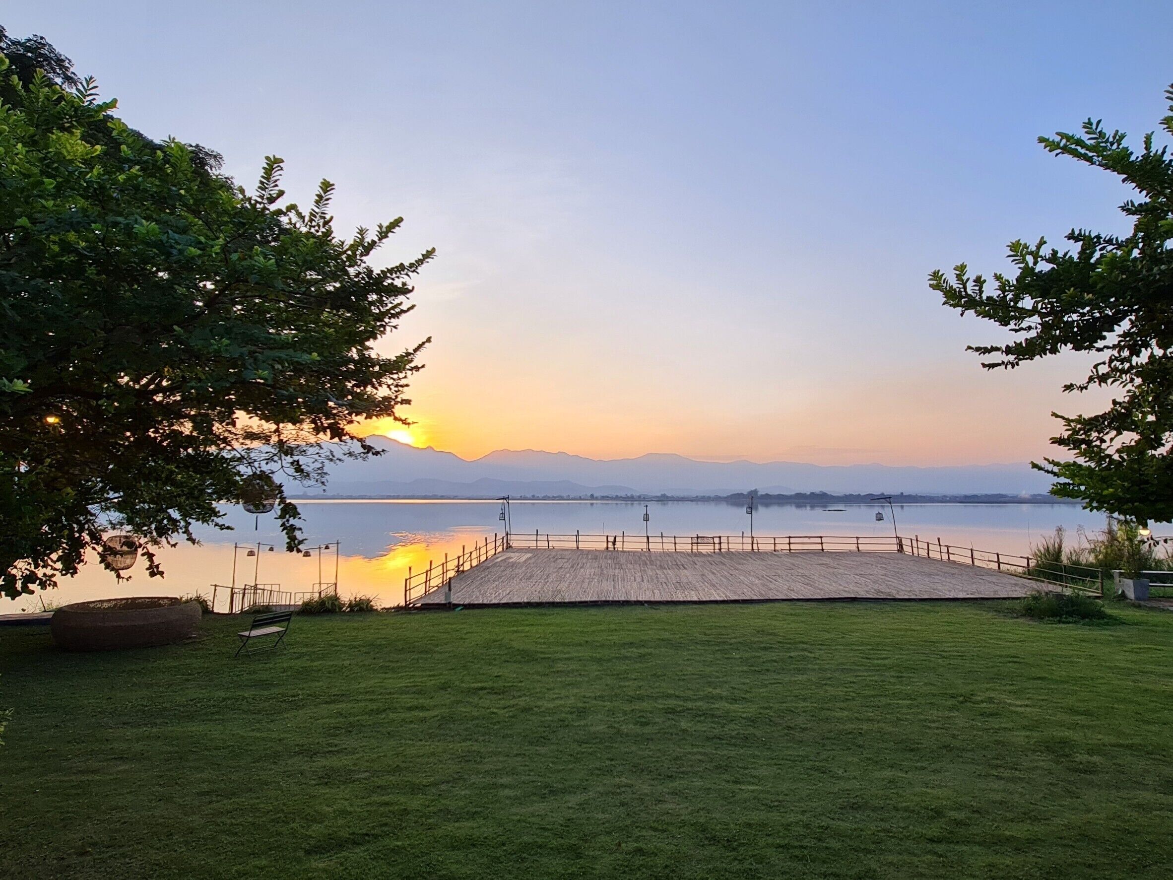A grassy area with a wooden dock extending into a calm lake, surrounded by trees.