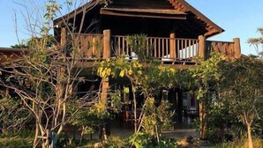 A wooden cabin with a balcony, surrounded by a garden with various plants and a stone pathway. - Naga Tara Resort (Phayao)