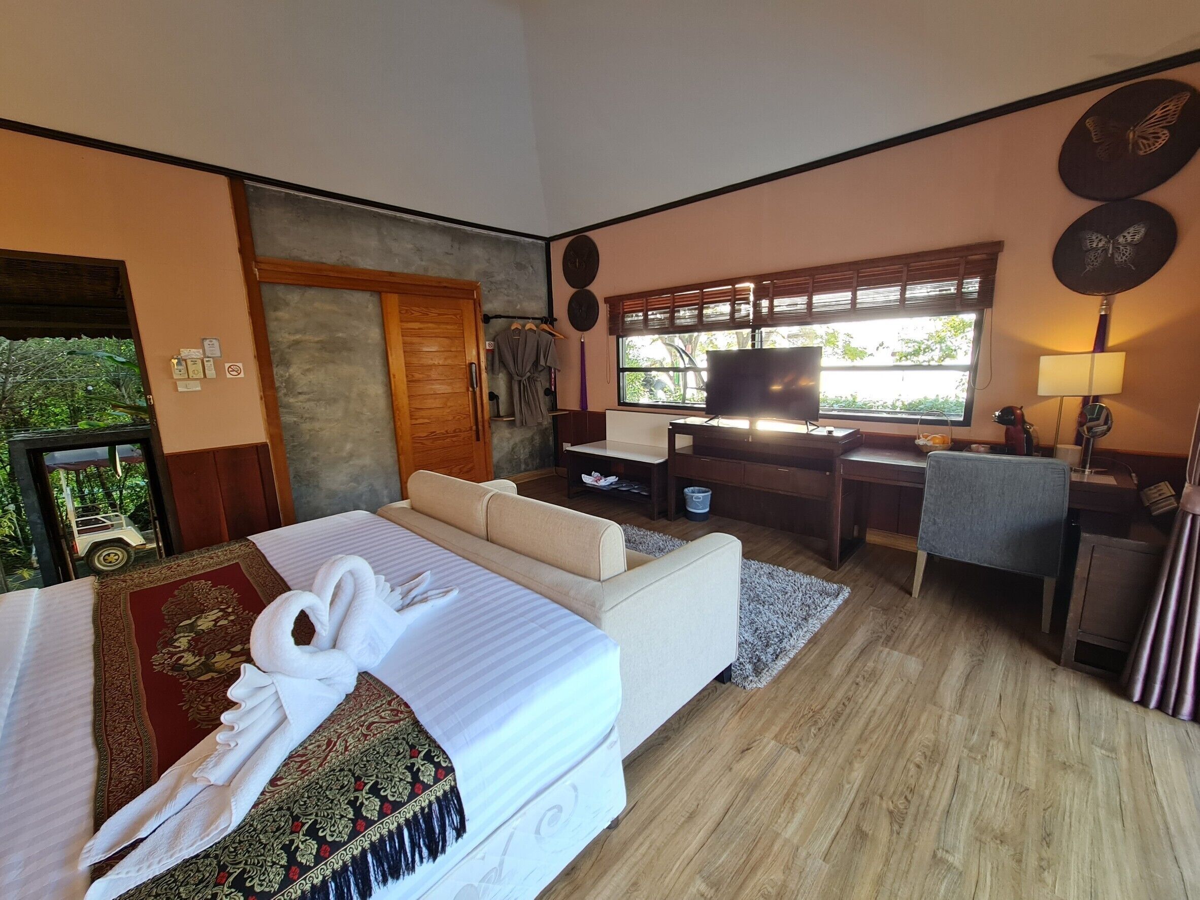 Ein Hotelzimmer mit Bett, Schreibtisch, Fernseher und einem Fenster mit Blick auf Grünflächen.