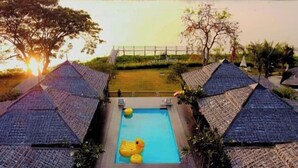 A pool with a duck float, surrounded by thatched-roof structures, overlooking a body of water. - Naga Tara Resort (Phayao)