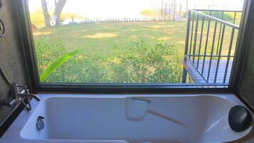 A bathroom with a bathtub, a window, and a view of a grassy yard.