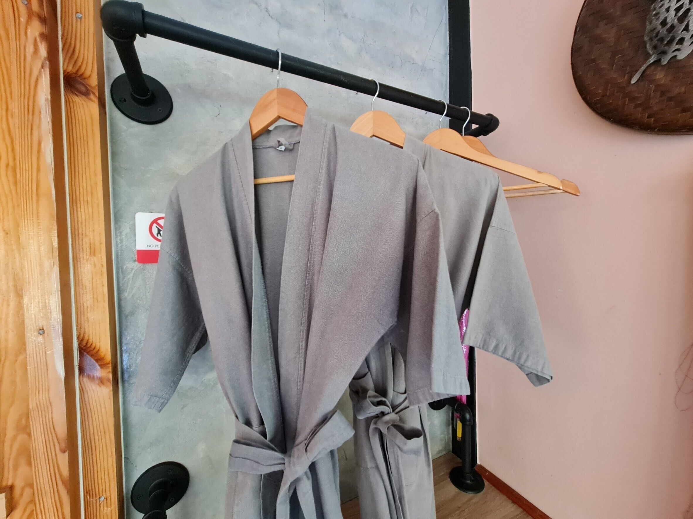 Een kamer met een houten deur, een metalen rek met kleding en een bordje 'No Pets'.