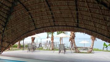 A poolside area with a thatched roof, lounge chairs, and umbrellas.