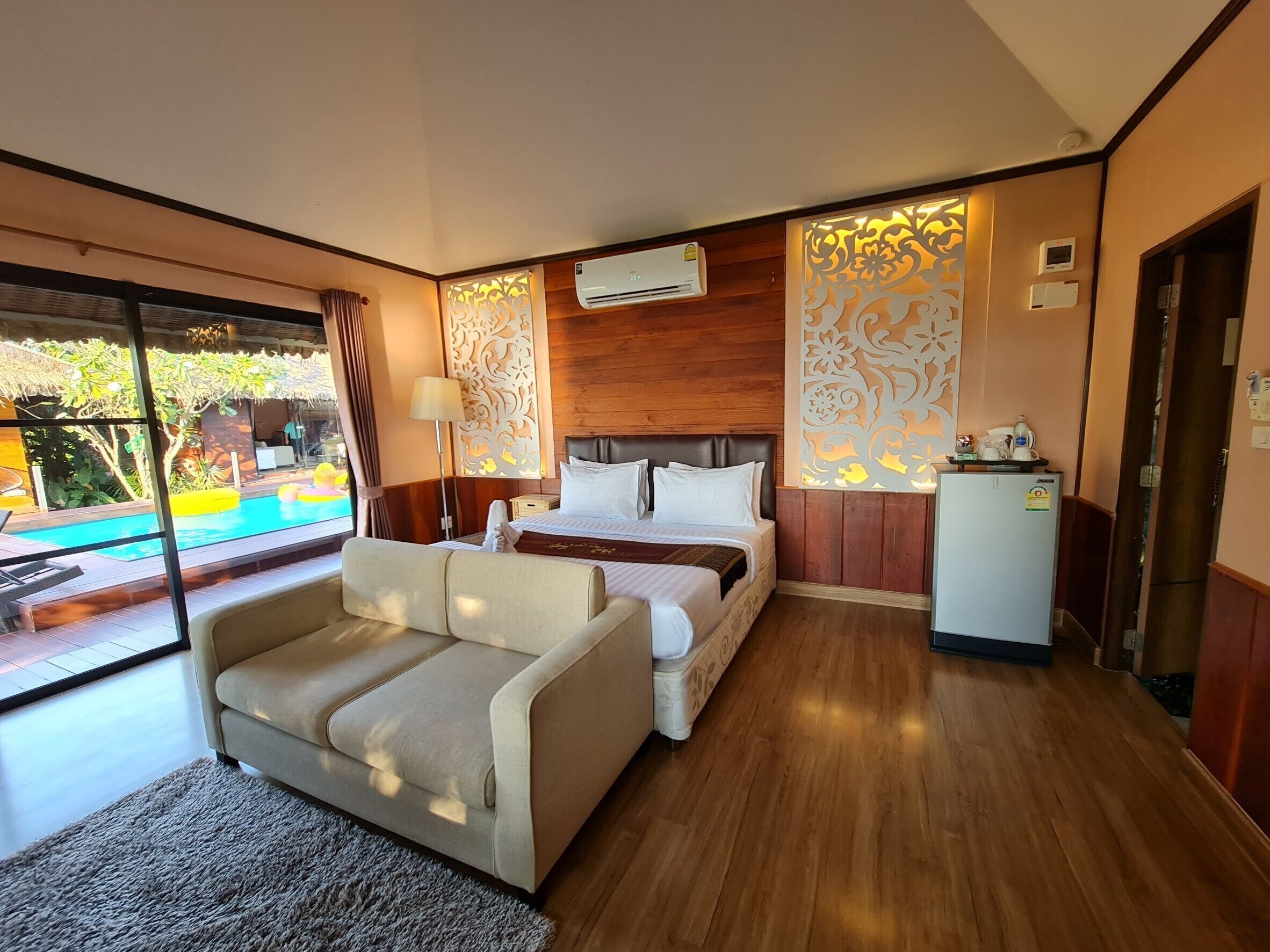 Habitación de hotel con cama, sofá, una mesita y vista a una piscina al aire libre.