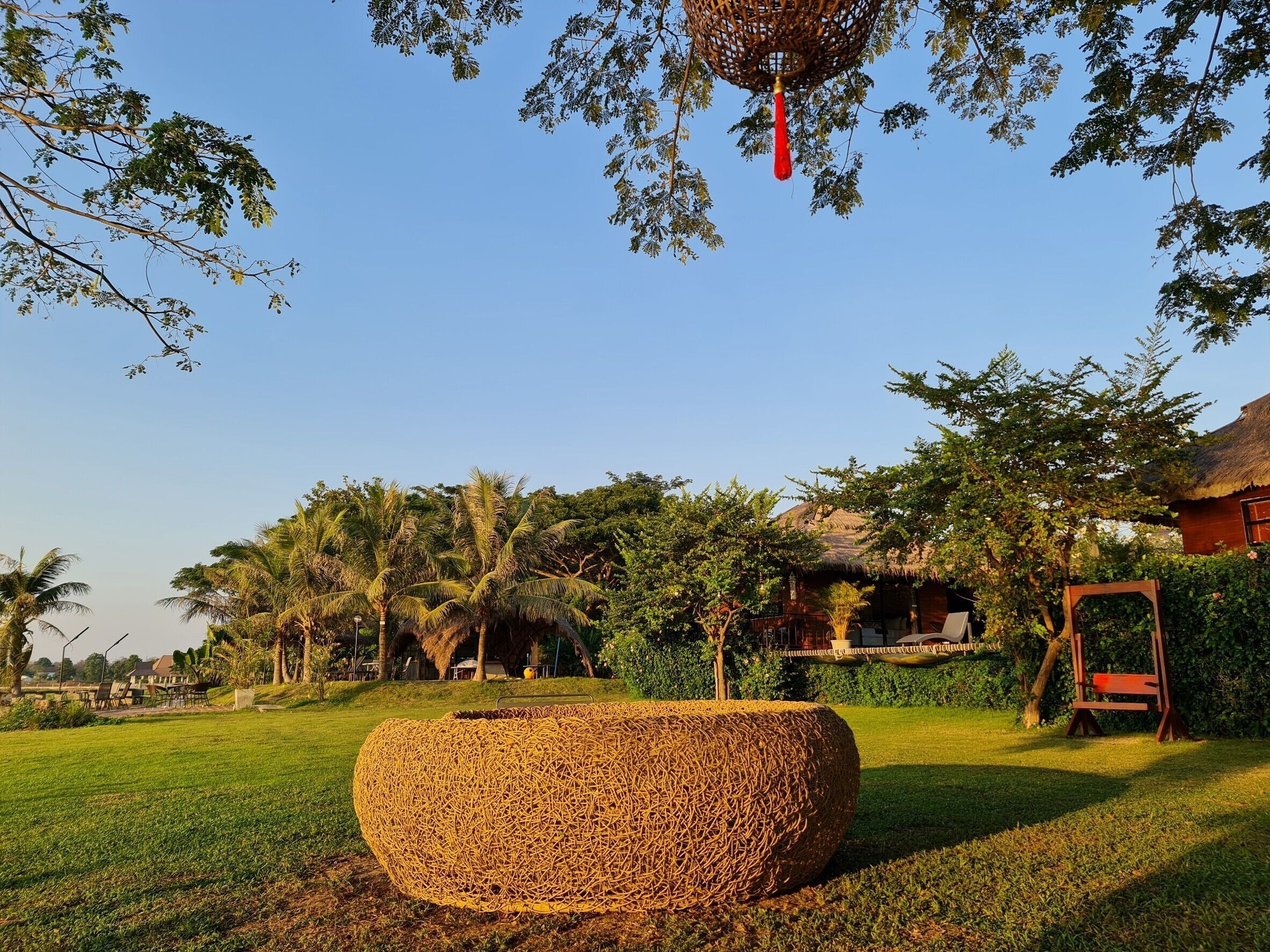 Un jardín con una maceta grande tejida, un edificio de techo de paja y un parque infantil.