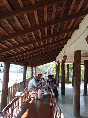 A covered outdoor dining area with wooden beams and pillars, tables, and chairs.