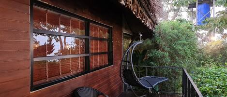 Una terraza de madera con mesa y sillas, techo de paja y vista a la vegetación.