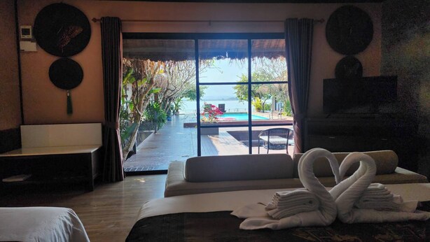 A hotel room with a bed, a sofa, a view of a pool, and a dining area. - Naga Tara Resort (Phayao)