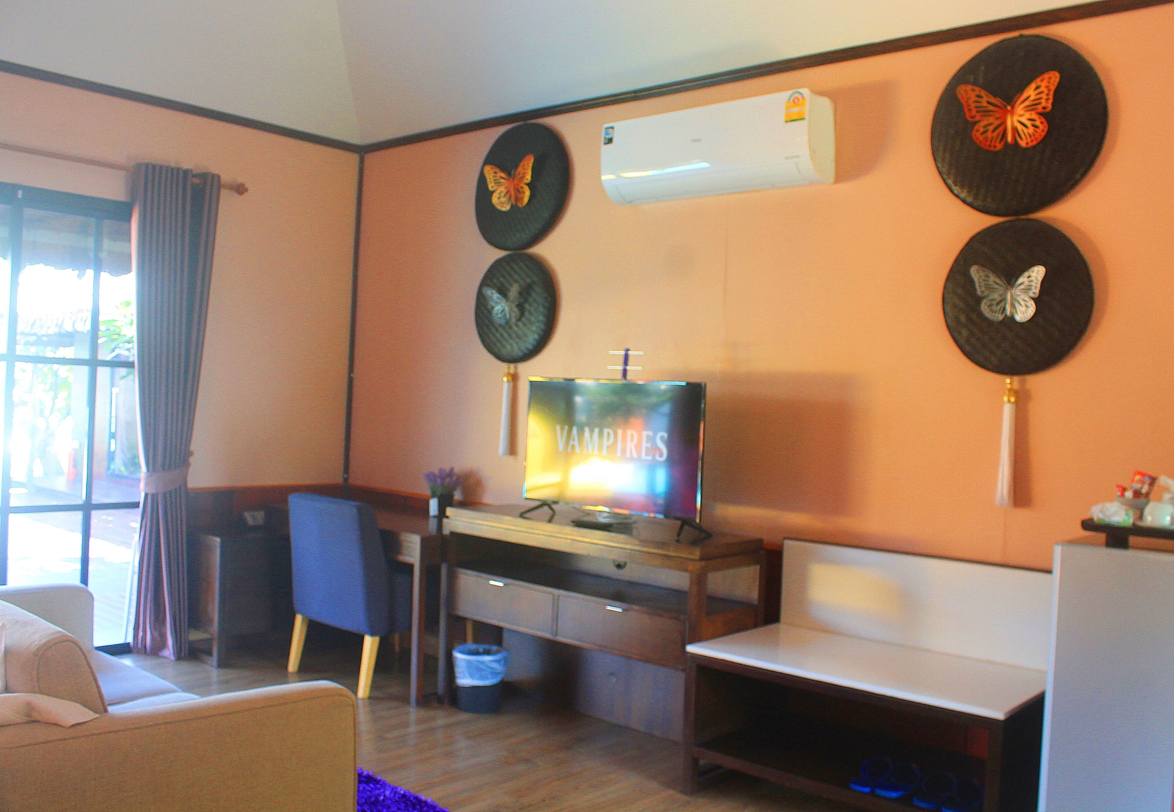 A living room with a TV, a sofa, a chair, a small table, and decorative butterfly wall art.