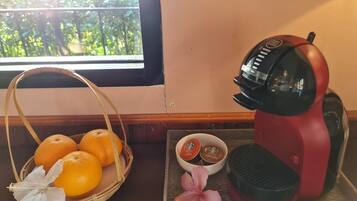A kitchen counter with a coffee maker, a basket of oranges, and a tray with coffee pods and a flower.
