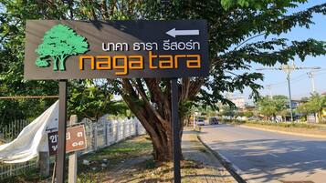 A directional sign with a tree and text, a sidewalk, and a road.