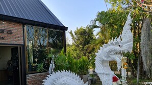 A building with a brick facade and large windows, surrounded by lush greenery and a white dragon sculpture. - Naga Tara Resort (Phayao)