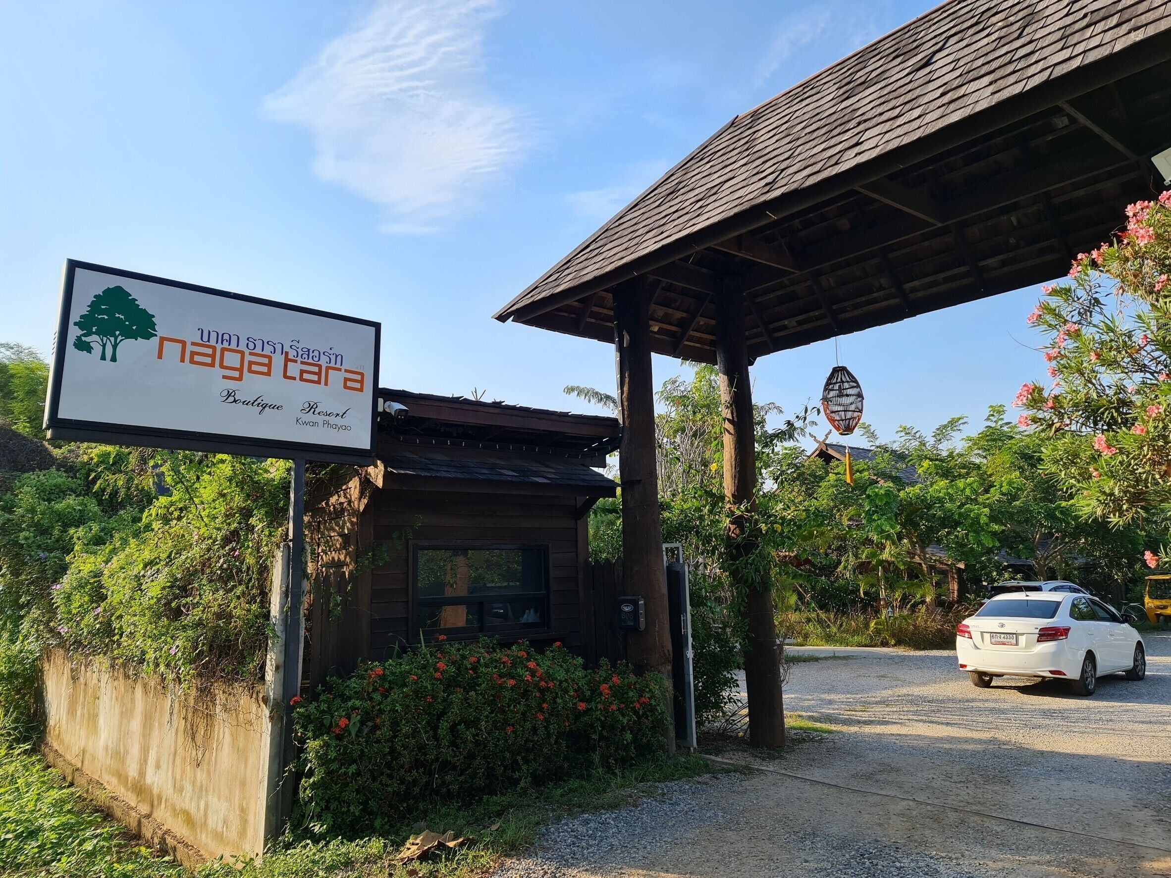 Señalización para 'Naga Tara Boutique Resort', con una estructura de madera y un coche estacionado cerca.