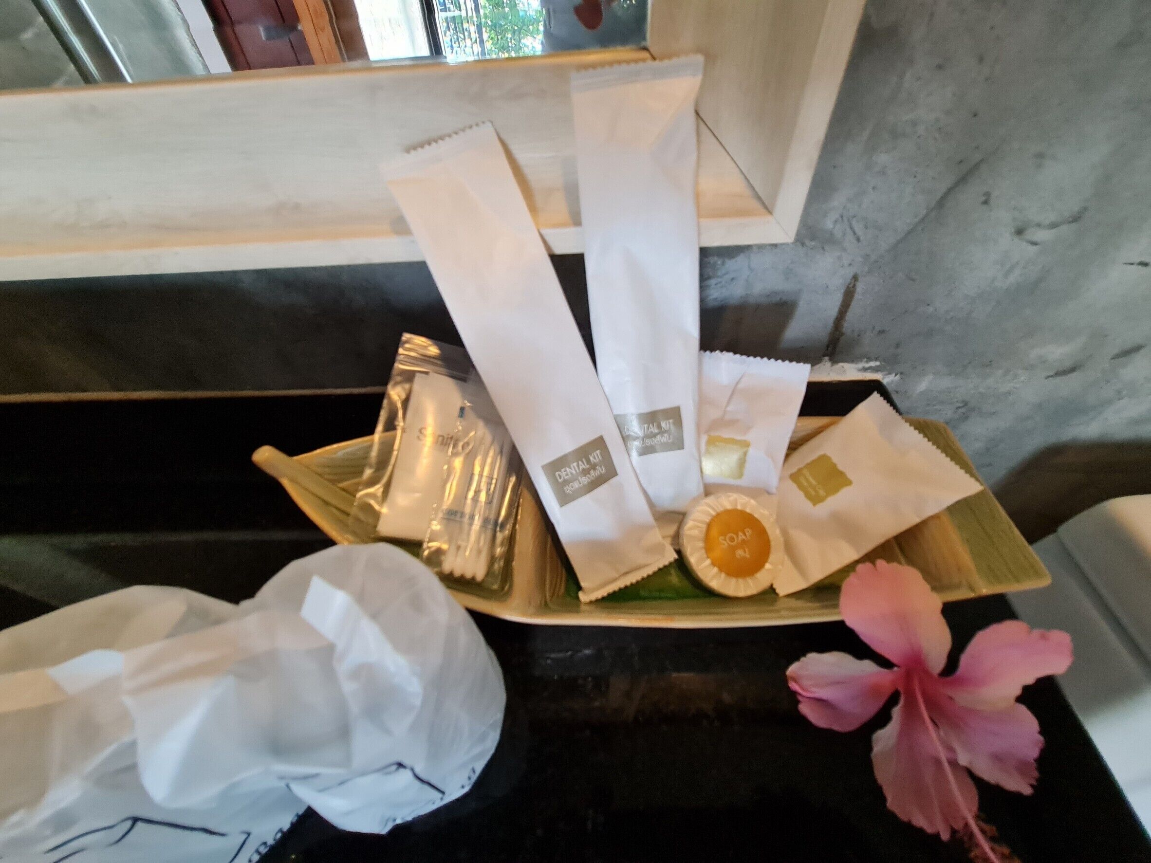 A tray with toiletries including a toothbrush, toothpaste, and a soap bar, placed on a wooden surface with a pink flower.