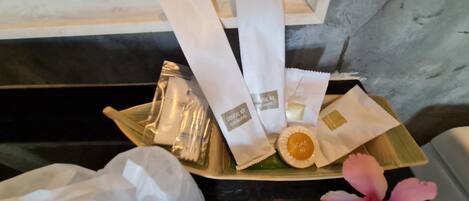 A tray with toiletries including a toothbrush, toothpaste, and a soap bar, placed on a wooden surface with a pink flower.