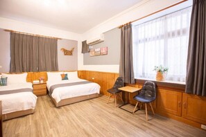 Habitación de hotel con dos camas, una mesita, dos sillas, un ventanal con cortinas, un equipo de aire acondicionado y una obra de arte colgada en la pared.