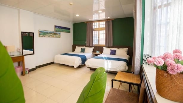 A hotel room with two beds, a small table, a chair, a window with curtains, and a wall-mounted mirror. - A Xin B&B (Jinning)
