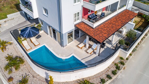 A modern multi-story building with a rooftop pool area, outdoor seating, and a red-tiled roof. - Urban Villa Penthouse (Podstrana)